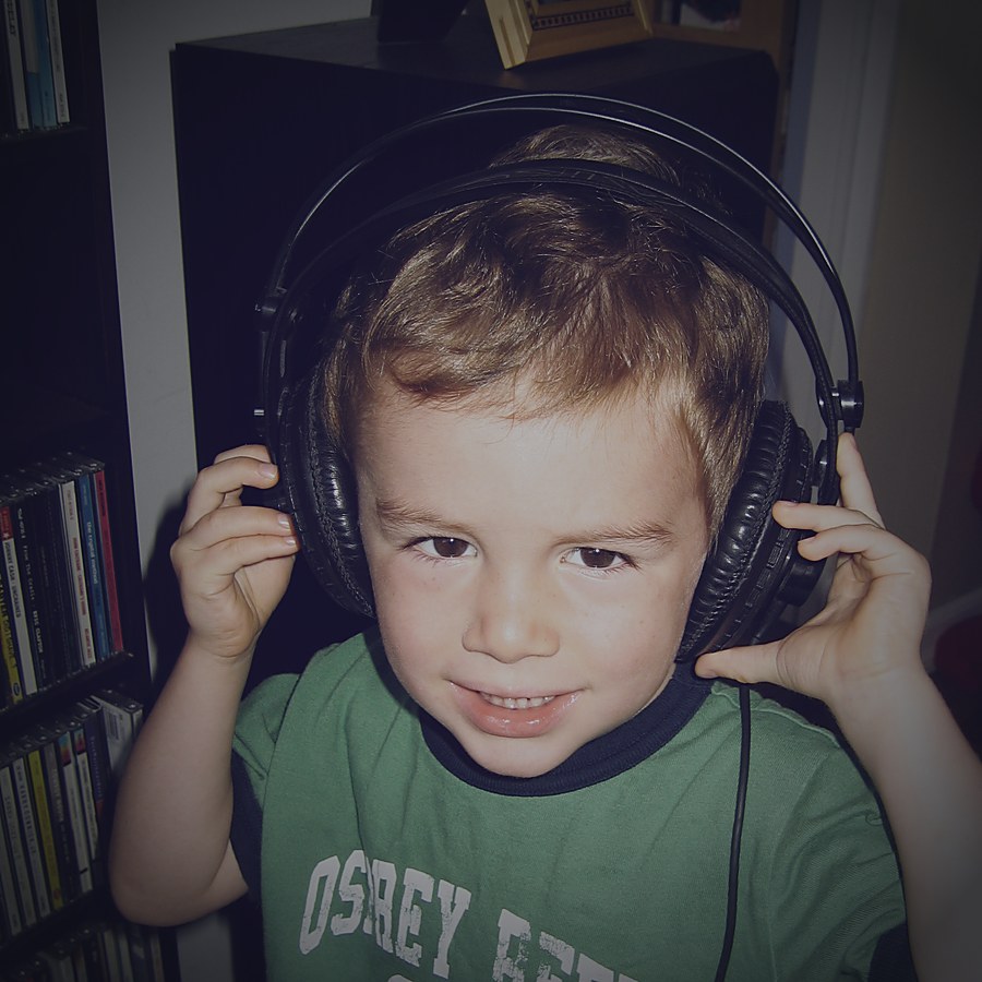 Kai Hansen as a young child wearing oversized studio headphones, in front of a wall of CDs and cassettes